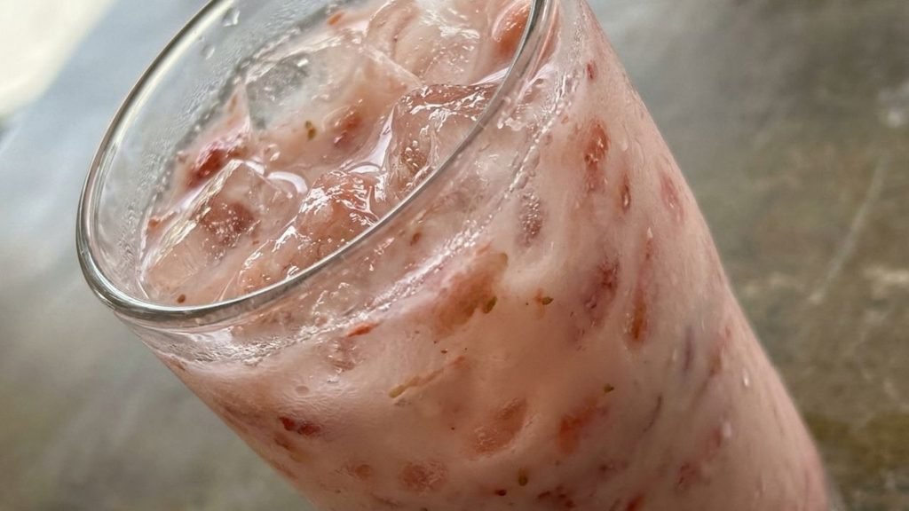 Close-up of ice and strawberry pieces in a pale pink coconut beverage.